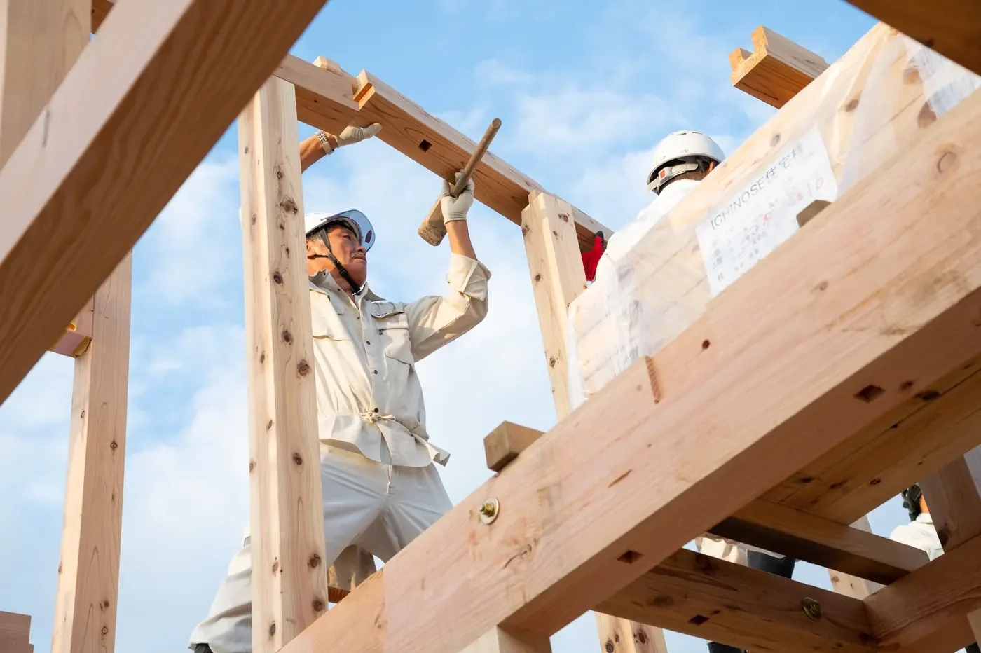 骨組みの上で、木槌を使って作業する大工たち